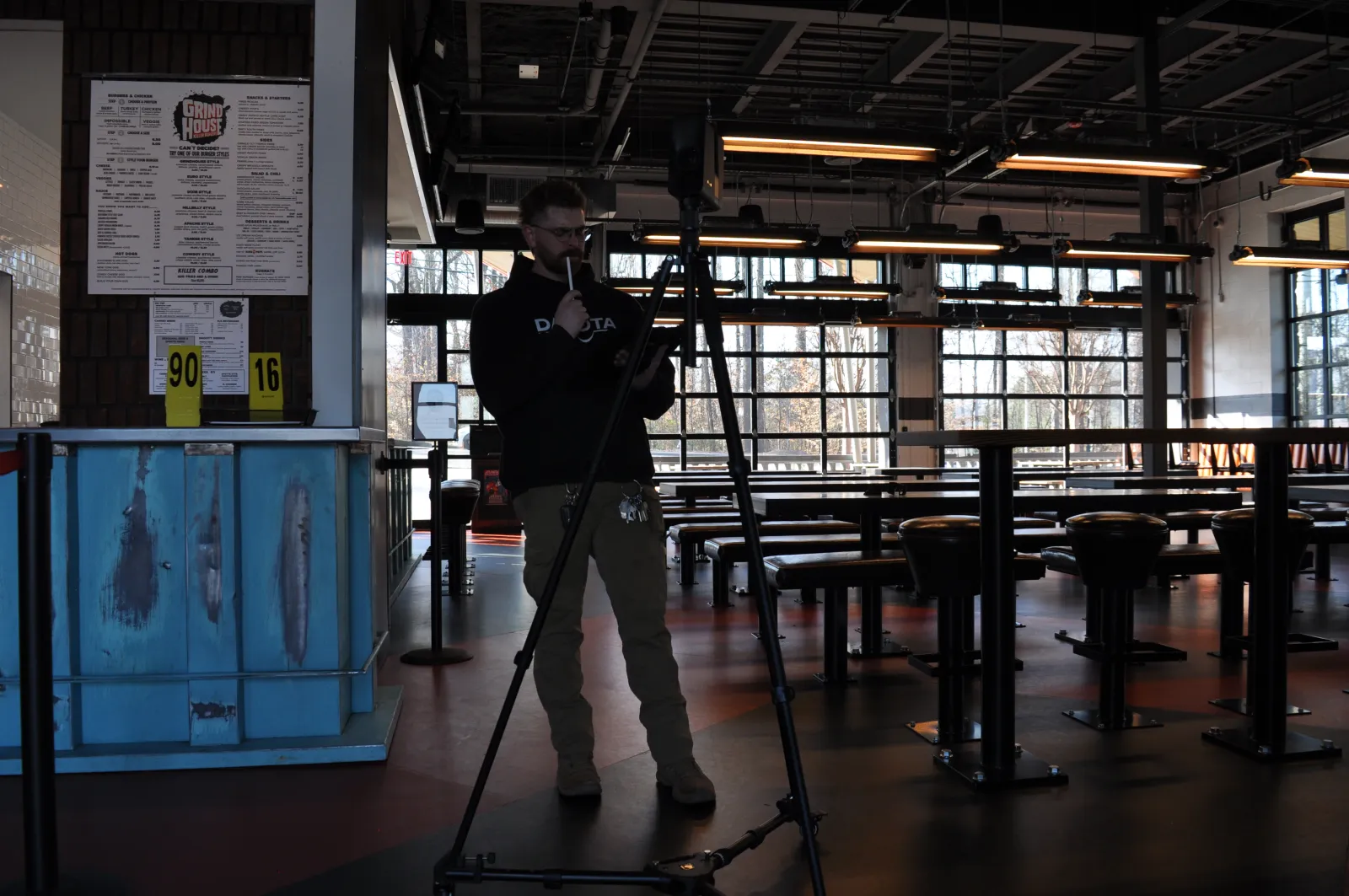 Man using camera tripod to record or photograph inside a dimly lit, modern industrial-style restaurant or cafe.