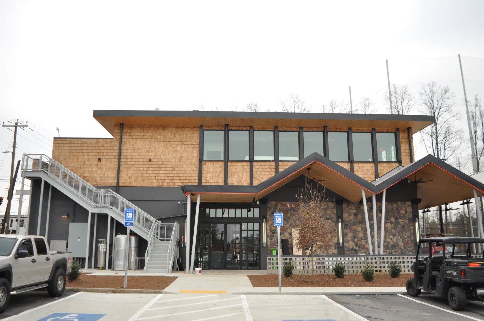 Modern two-story building with wooden accents, large windows, external staircase, and parked vehicles in front.