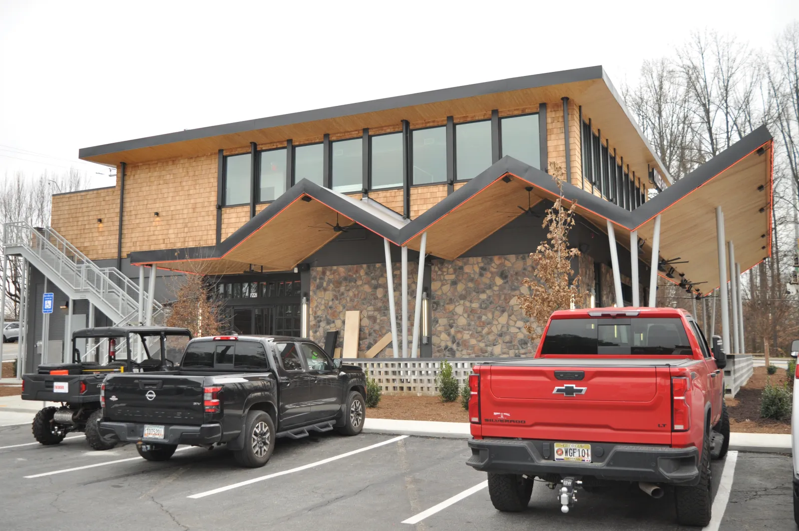 Modern two-story building with unique zigzag roof and parked black and red pickup trucks in front under overcast sky