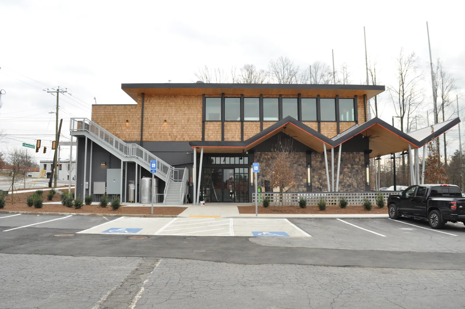 Modern two-story building with stone facade, wooden accents, angular roof, and adjacent parking with handicap spaces.