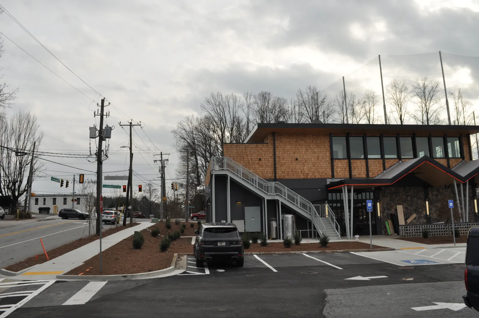 Modern two-story building with exterior staircase in parking lot under cloudy sky near a street intersection.
