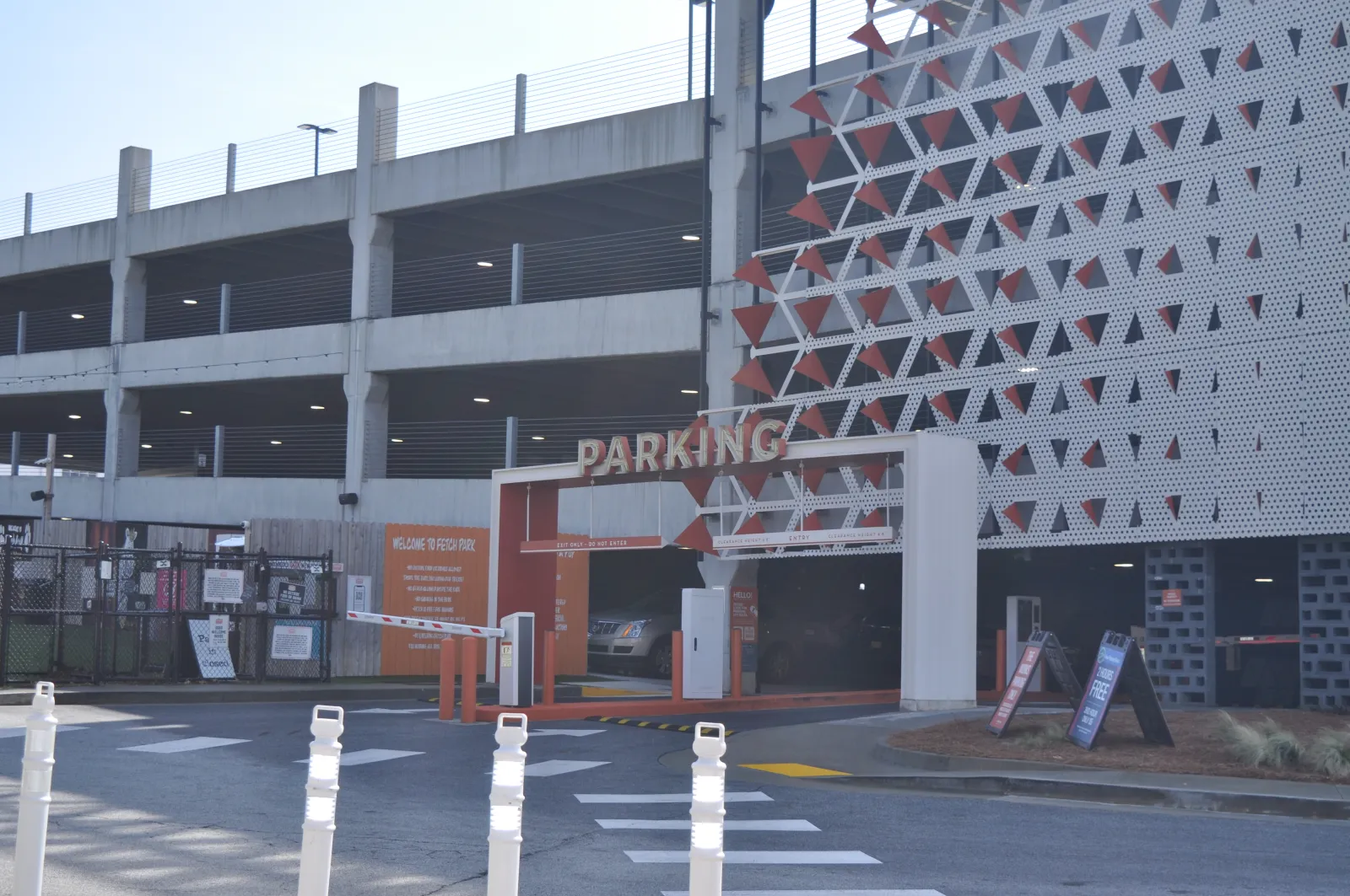 Multi-level parking garage entrance with a white and orange facade and parking barriers on a sunny day.