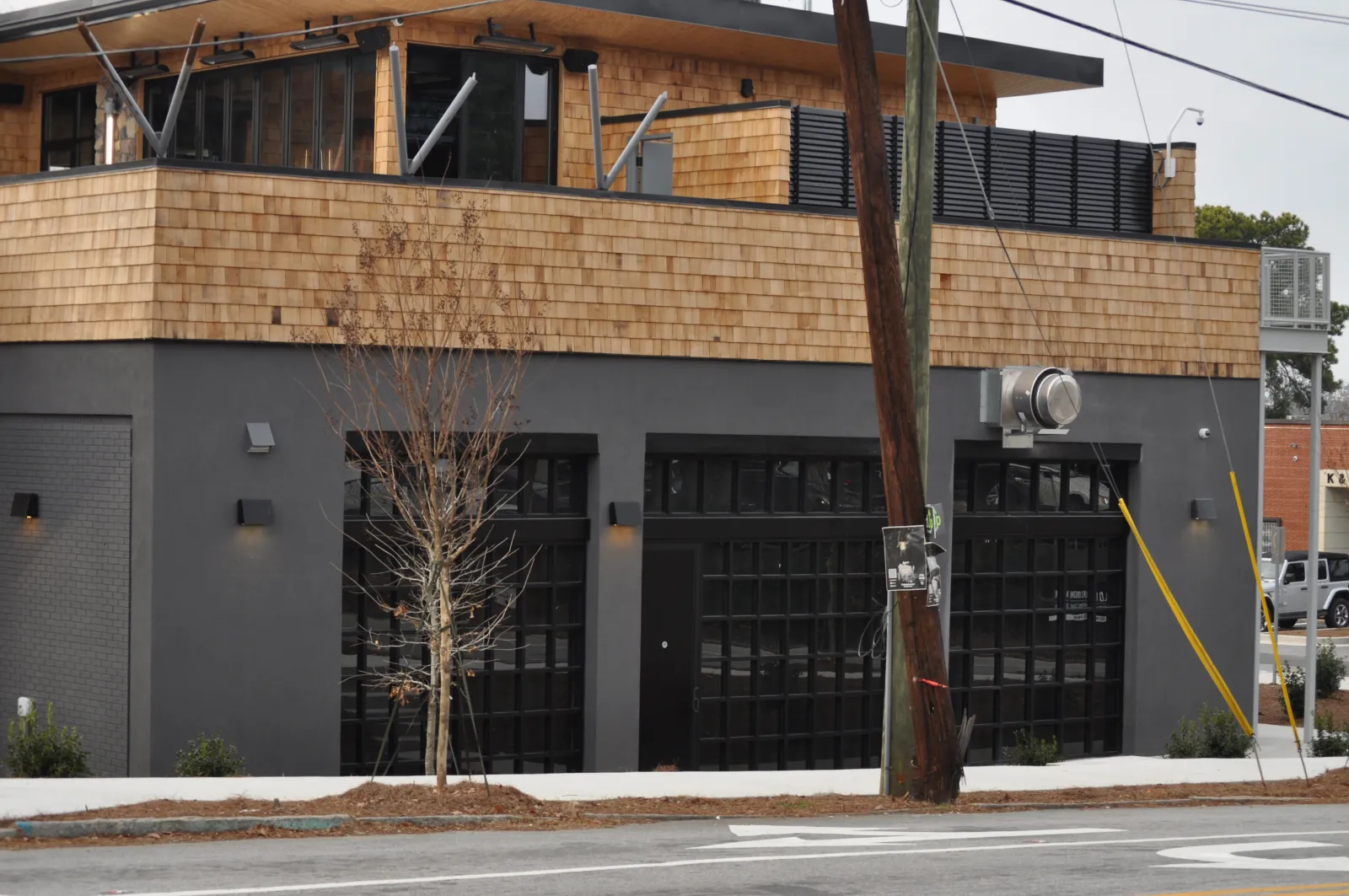 Modern two-story commercial building with gray walls, large black windows, and cedar shingle siding on upper floor.