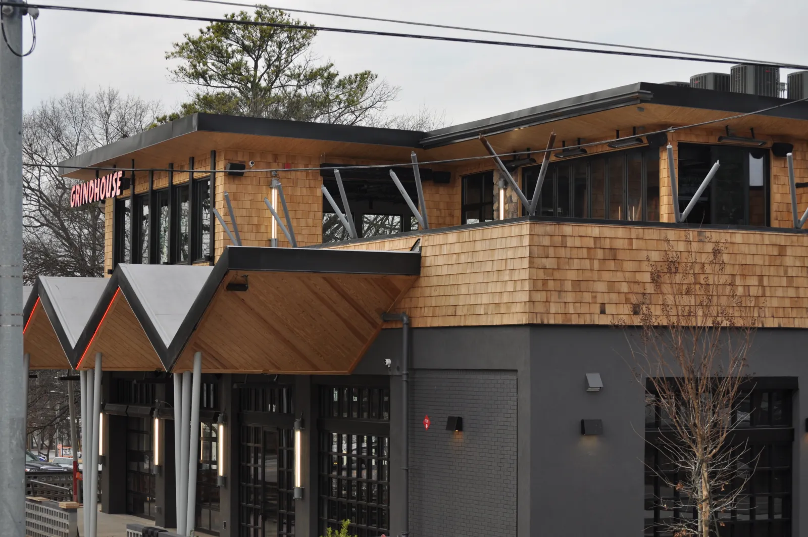 Modern two-story building with wood siding and large windows housing Grindhouse restaurant.