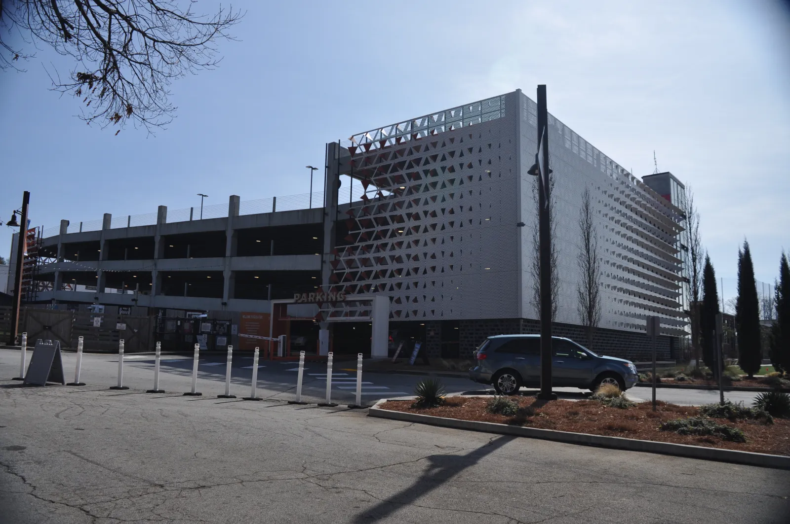 Modern multi-level parking garage with white perforated facade and a car parked outside on a sunny day