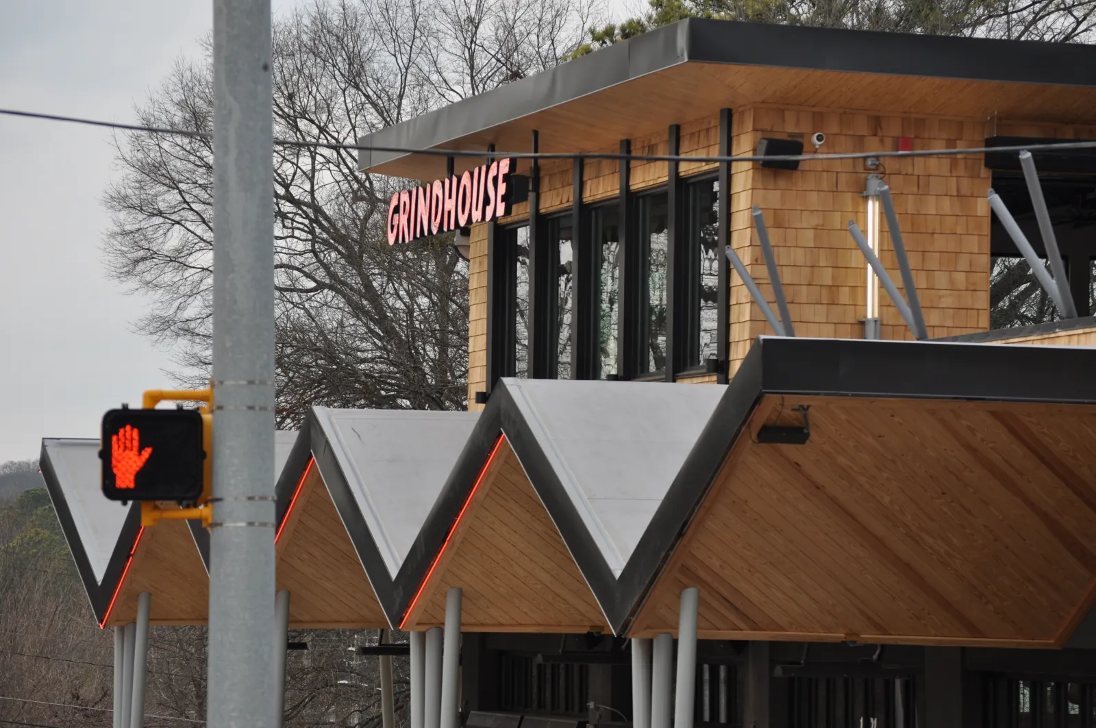 Modern Grindhouse building with zigzag roof and red neon sign beside a pedestrian stop light showing red hand