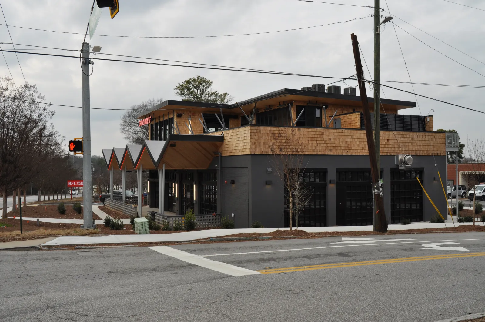 Modern two-story building with wooden accents and large windows on a cloudy day at a street corner.