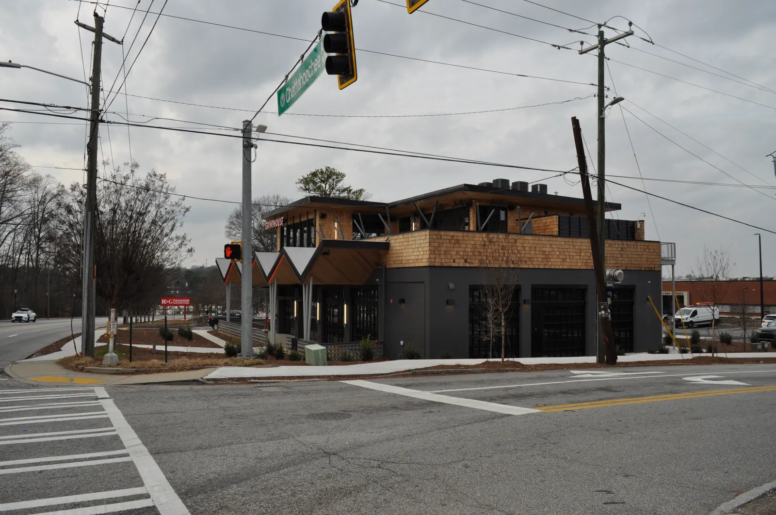 Modern two-story commercial building with wood accents at a city intersection on a cloudy day