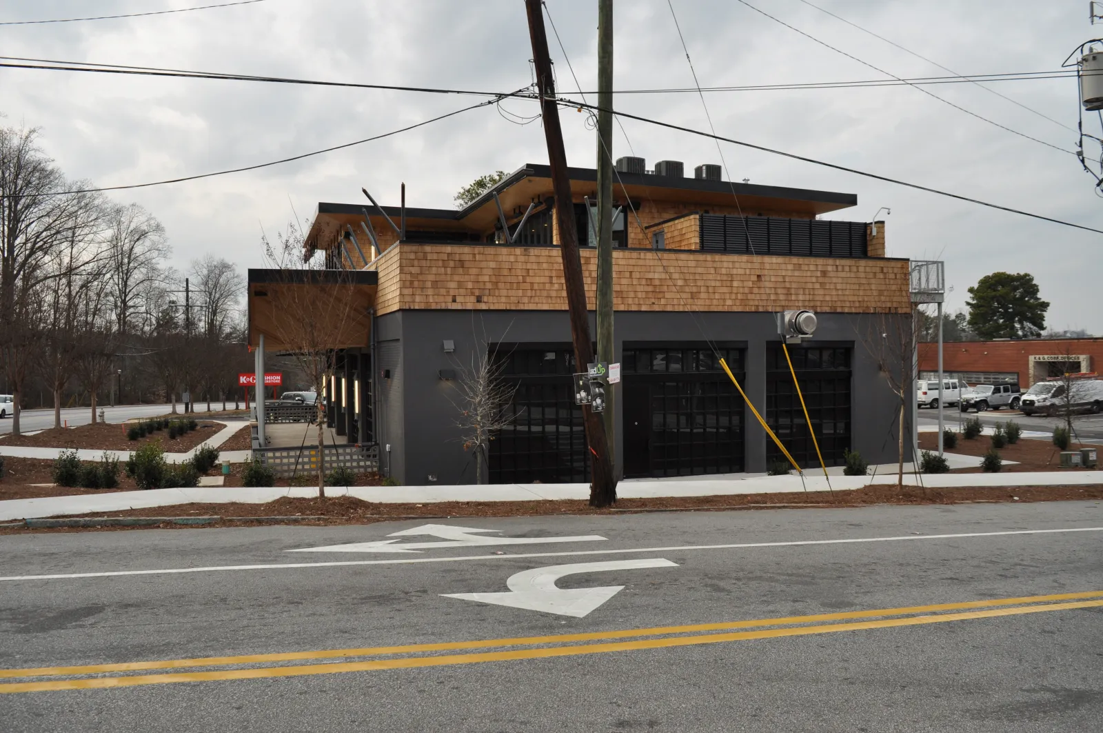 Modern two-story building with wood siding and black garage doors on a street with traffic arrows and overhead wires.