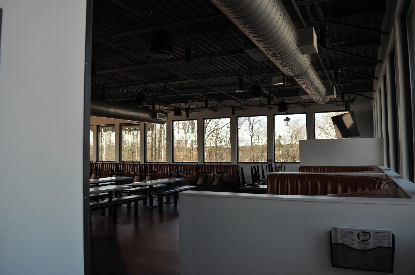 Empty modern restaurant dining area with large windows, high ceilings, and brown leather booths during daytime.