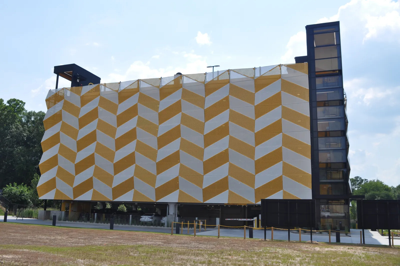 Modern building with yellow and white geometric patterned facade and glass elevator tower on a sunny day.