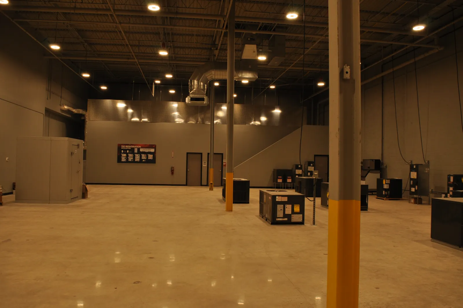 Spacious industrial warehouse interior with polished concrete floor, overhead lighting, and scattered equipment units.