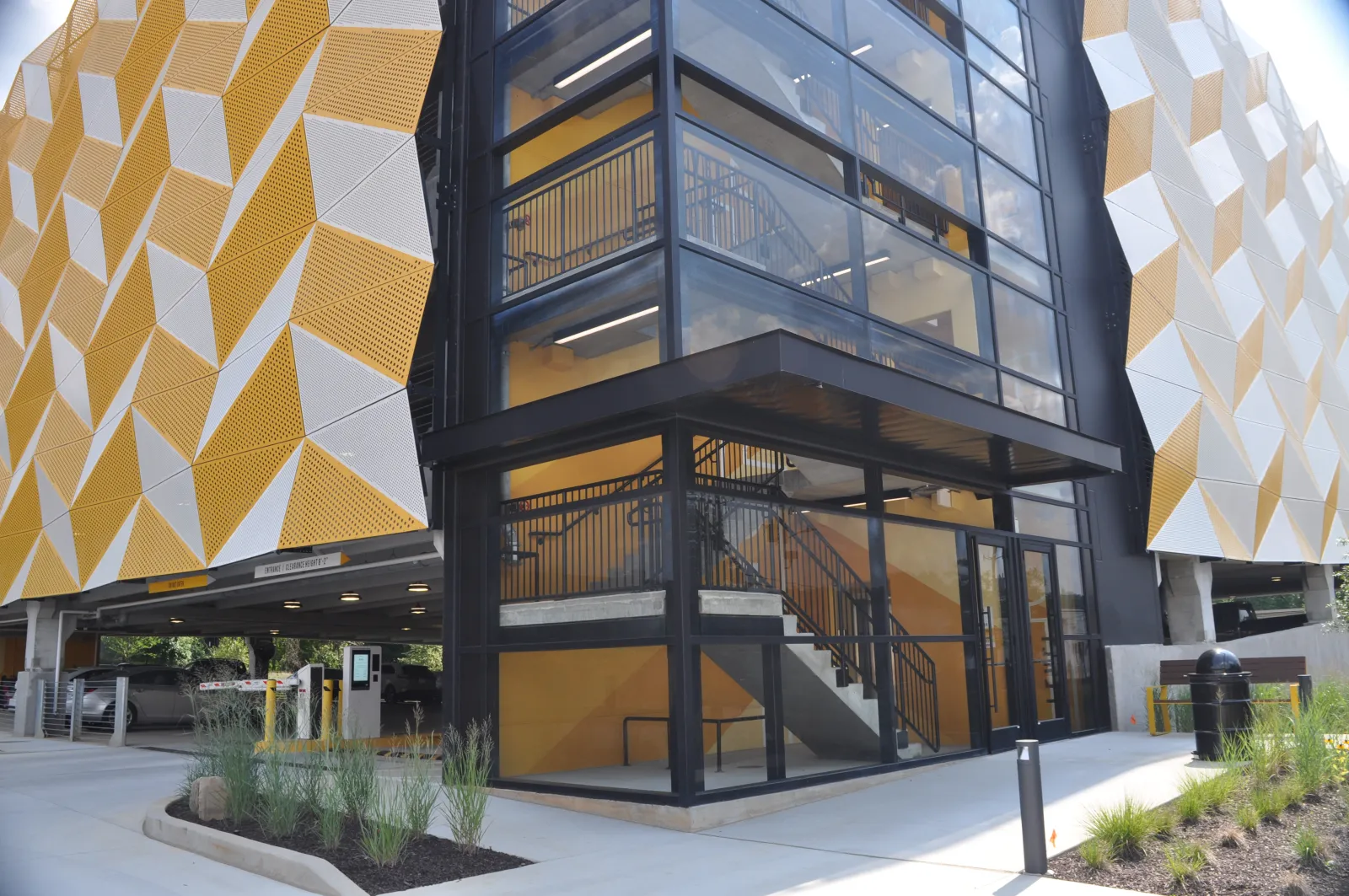 Modern parking garage with yellow and white geometric patterned facade and glass-enclosed staircase.