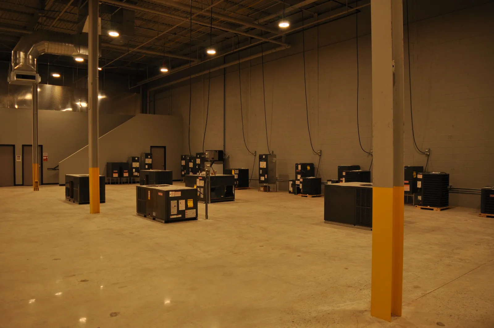 Spacious industrial warehouse with HVAC units on polished concrete floor and high ceiling with lighting.