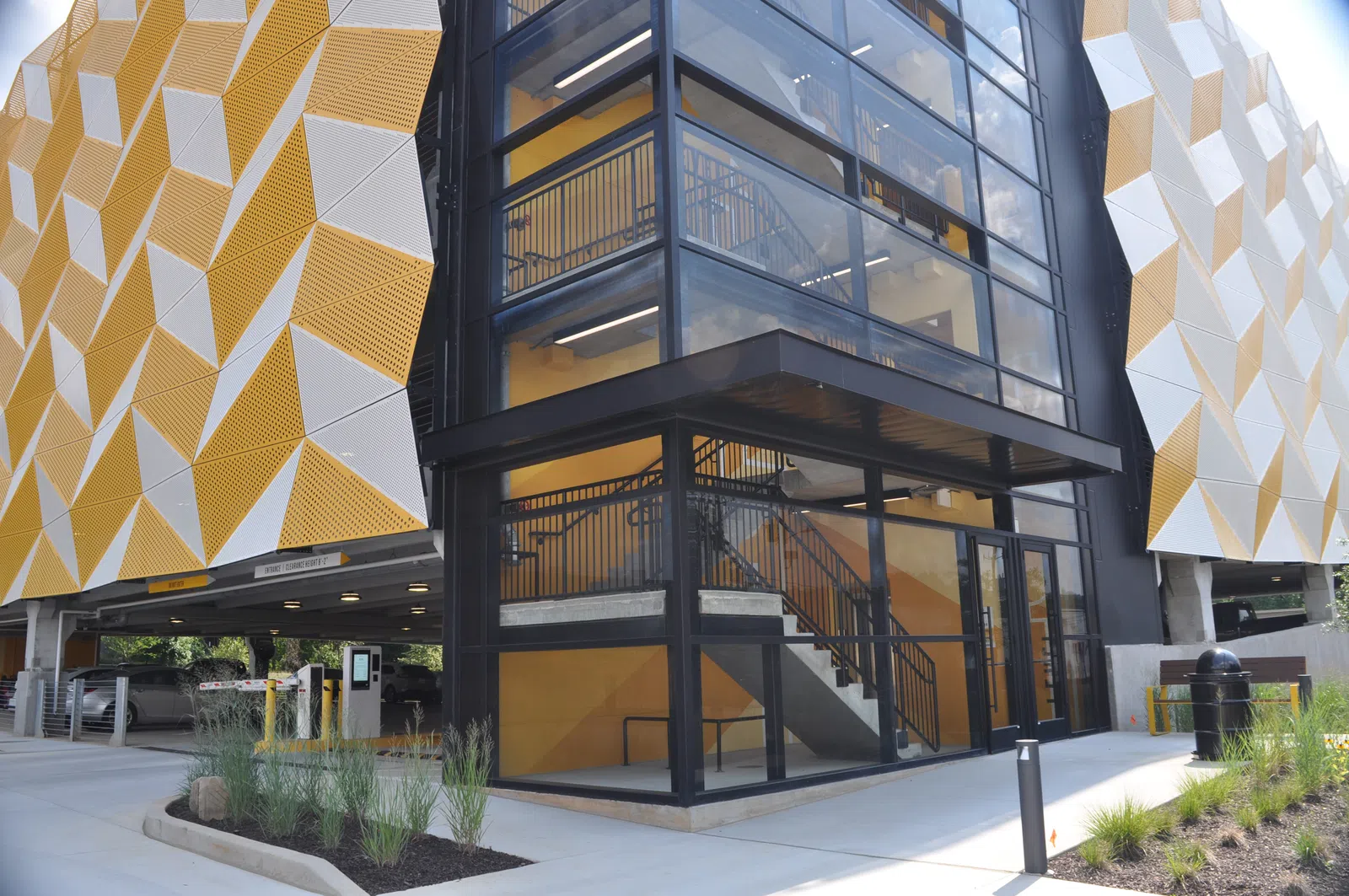 Modern parking garage exterior with geometric yellow and white panels and glass-enclosed stairwell.