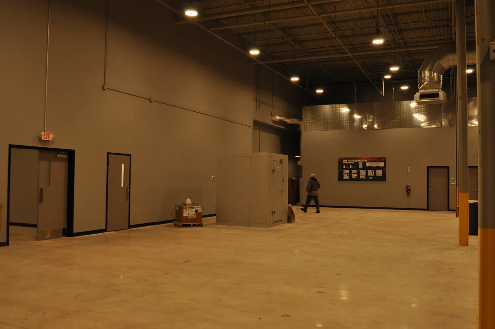Spacious empty industrial warehouse with smooth concrete floor, gray walls, high ceiling, and overhead lights.