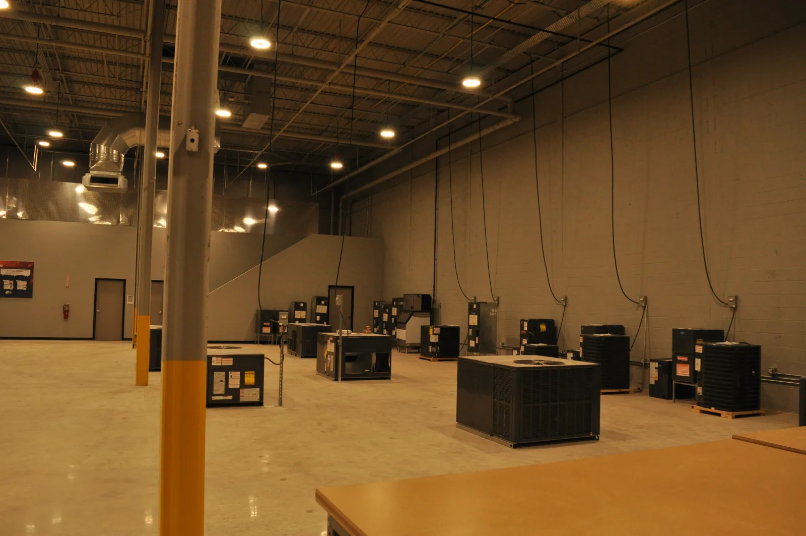 Spacious industrial warehouse with multiple HVAC units and high ceilings under bright overhead lights.