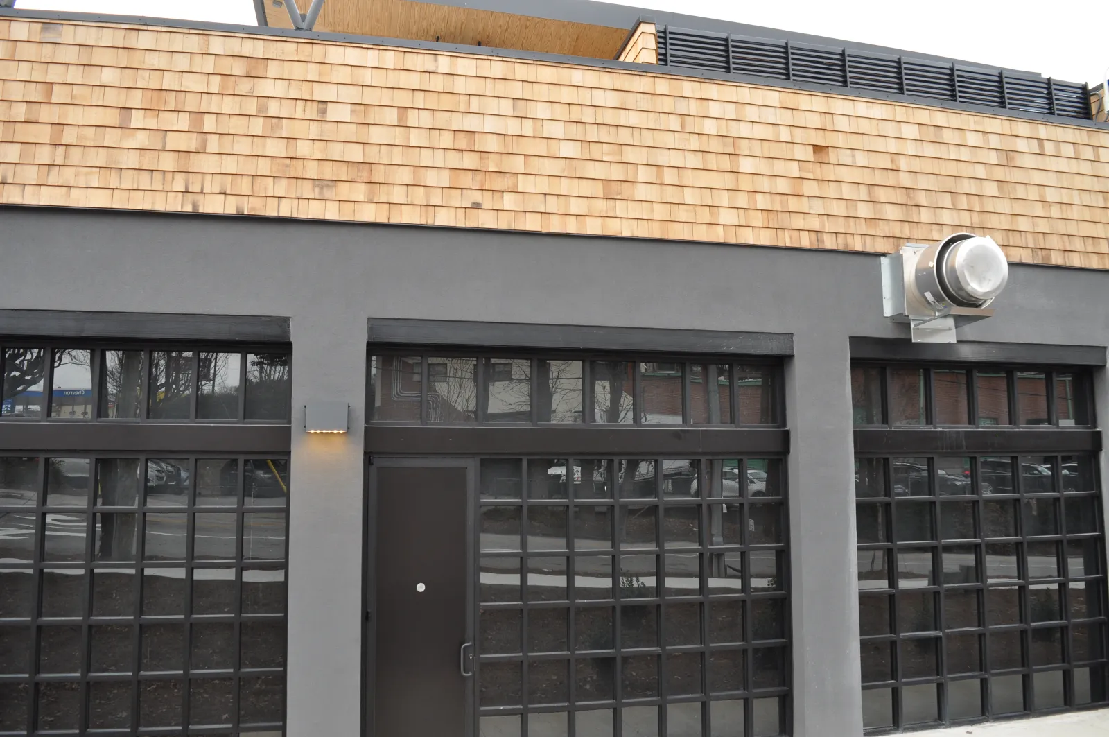 Modern commercial building facade with large grid windows, dark door, gray stucco, and wooden shingle trim.