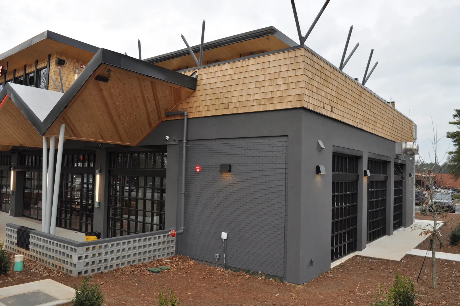 Modern commercial building with gray brick walls, wooden accents, large windows, and geometric roof design