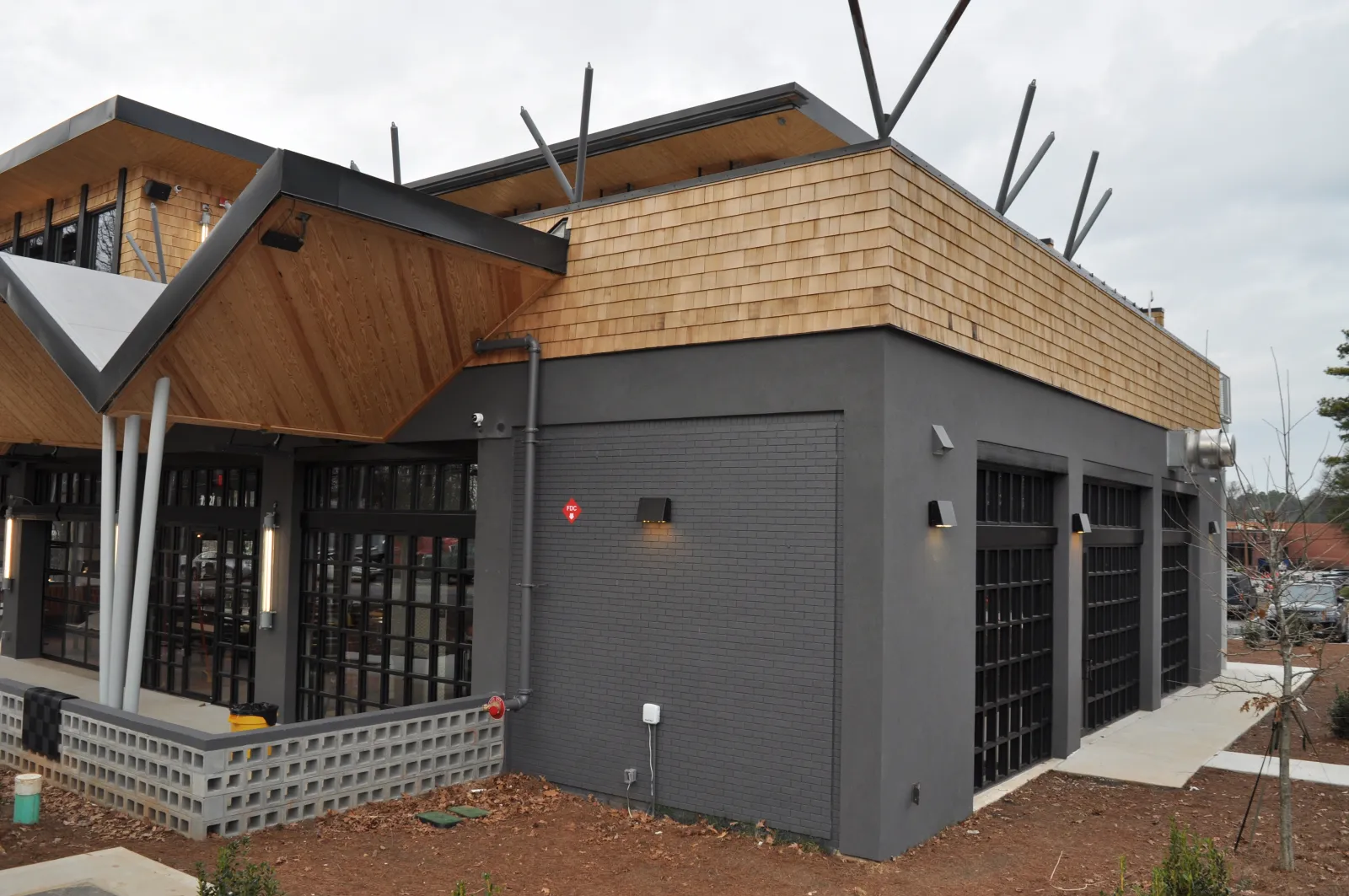 Modern commercial building with dark gray brick walls, wood shingles, large windows, and unique angled roof design.