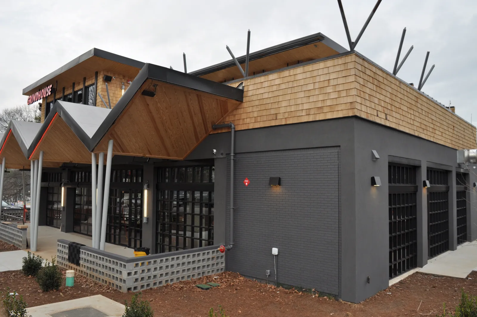 Modern restaurant building with black brick walls, large windows, and wooden shingle roofing under gray sky