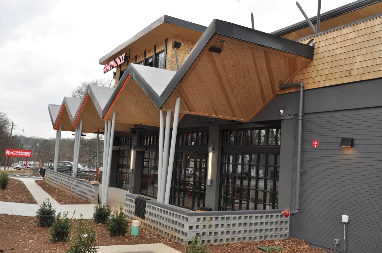 Modern building exterior with angled wooden roof panels, large glass windows, and landscaped surroundings on a cloudy day