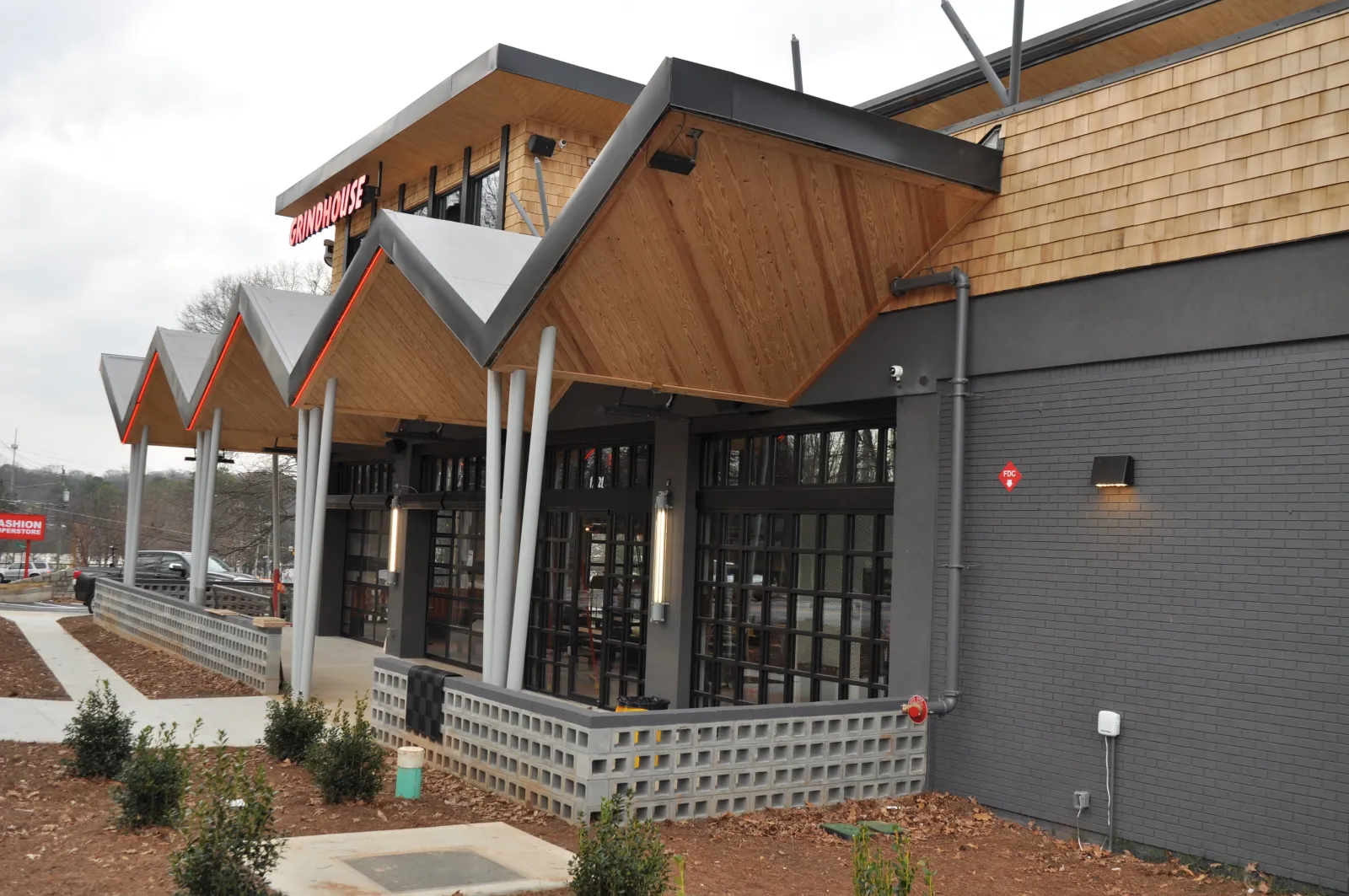 Modern restaurant exterior with zigzag wooden roof, large windows, and landscaped walkway under cloudy sky