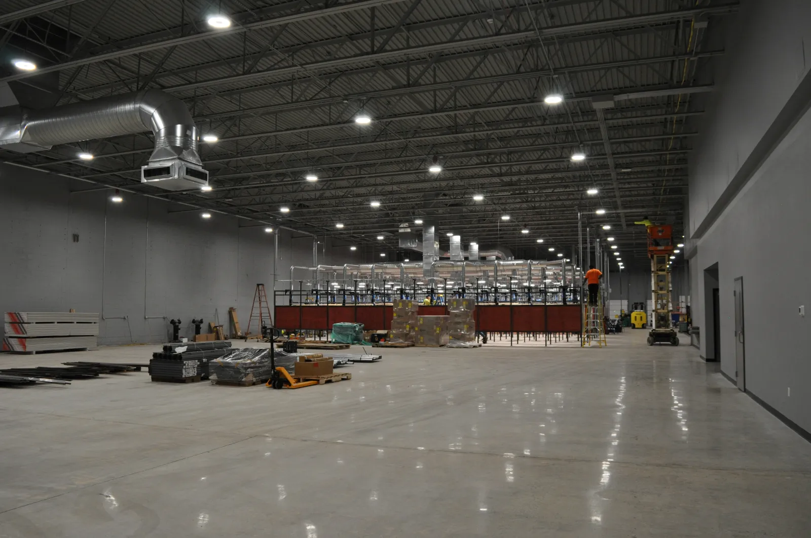 Spacious industrial warehouse under construction with high ceilings and suspended ductwork and lighting