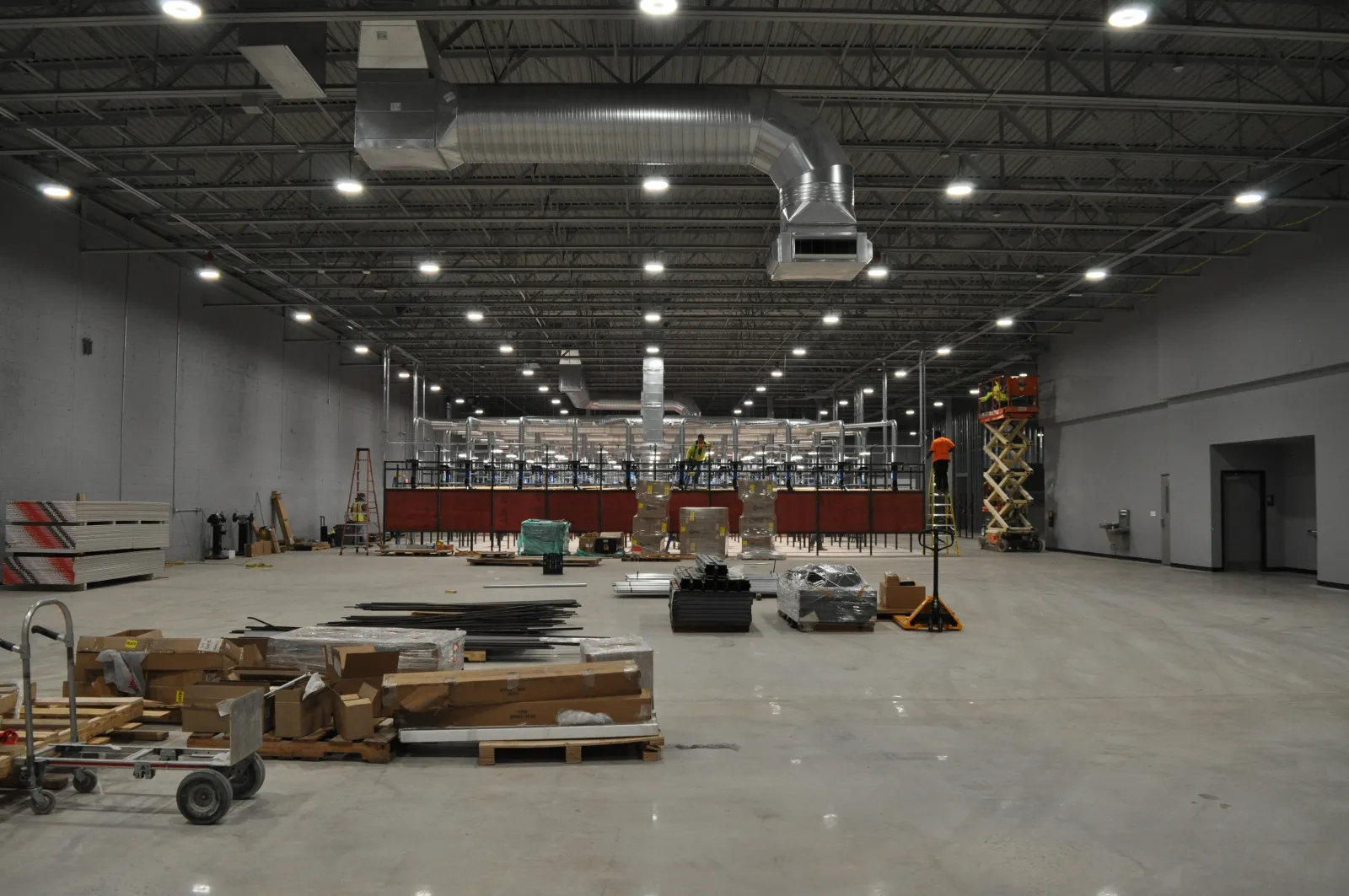 Interior of a large industrial warehouse under construction with materials and equipment scattered on polished concrete floor.