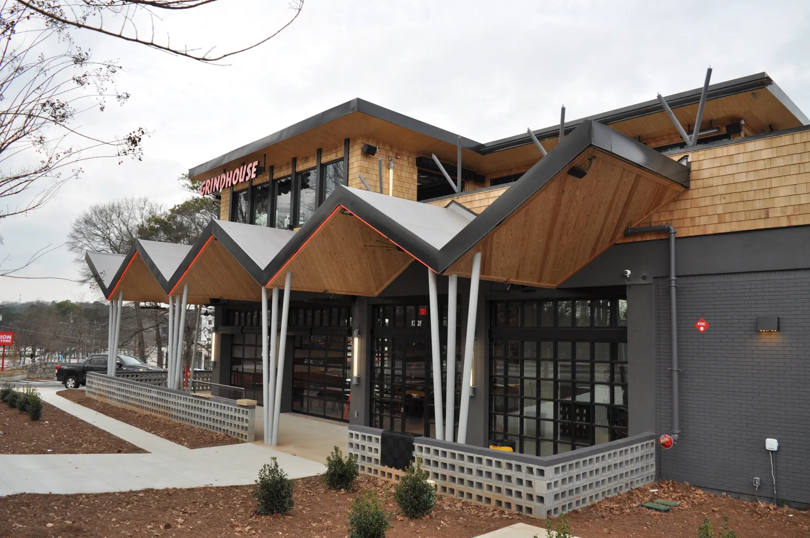 Modern restaurant exterior with geometric roof design, wooden accents, large windows, and landscaped surroundings.