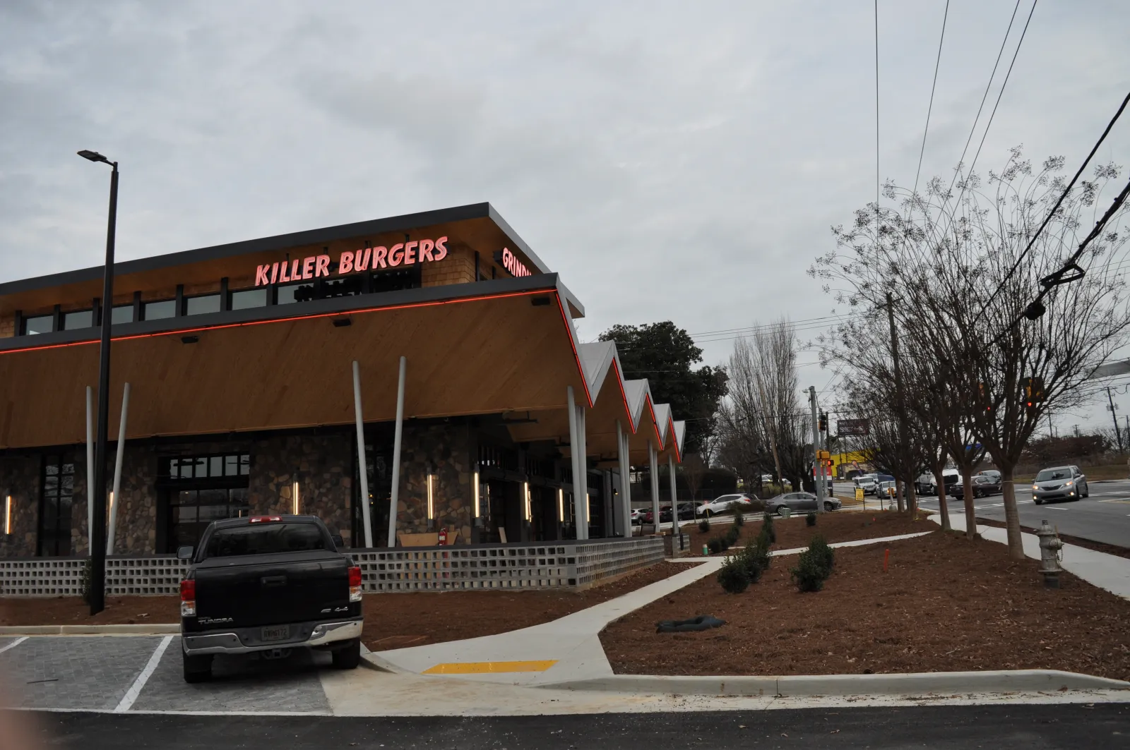 Modern Killer Burgers restaurant with distinctive peaked roof and cloudy sky, parked truck, and street view.