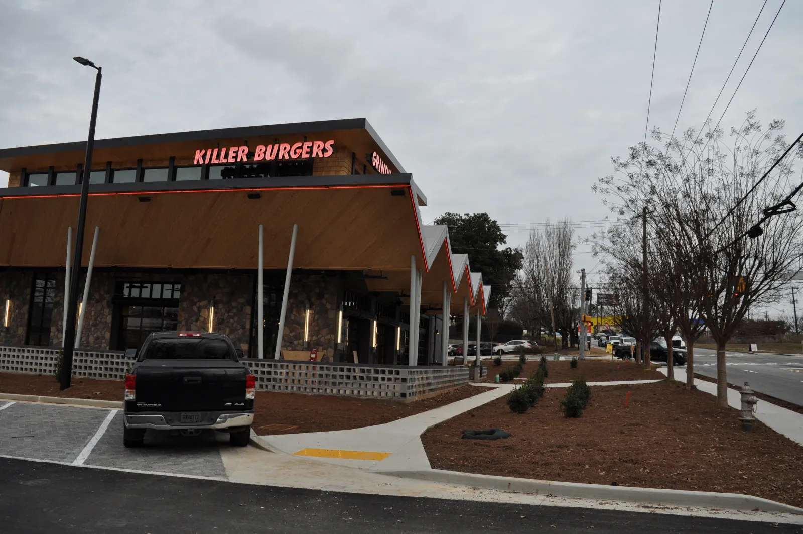 Killer Burgers restaurant exterior with neon sign during cloudy day and parked black pickup truck