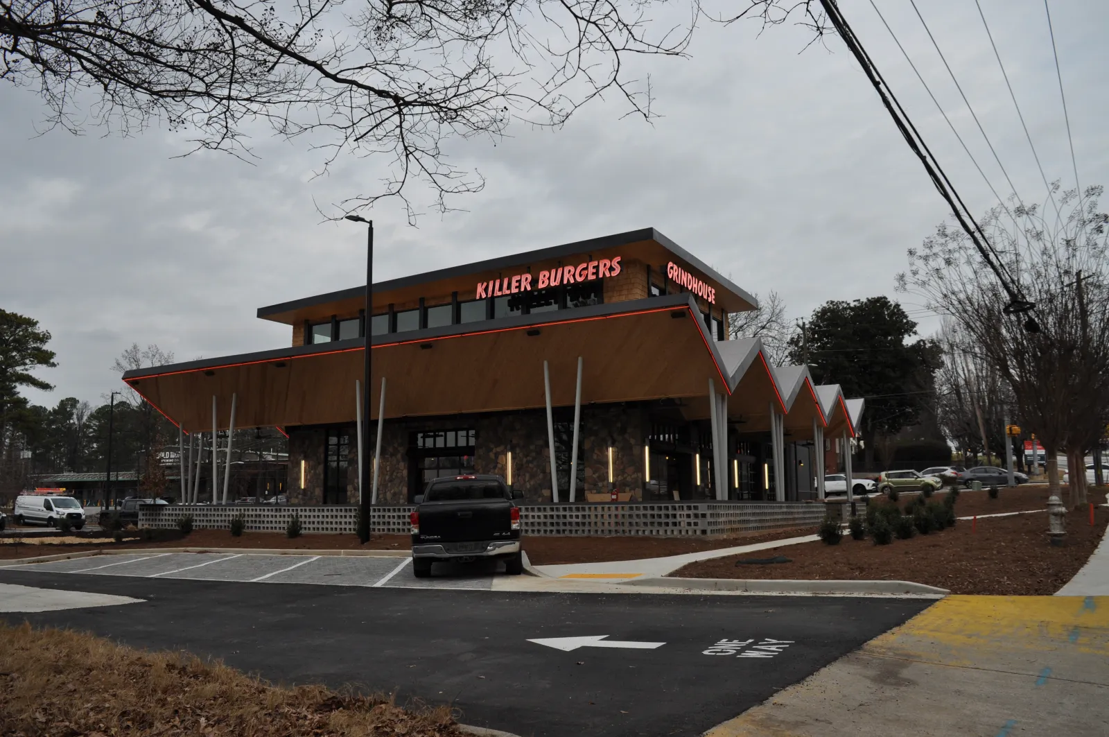Modern two-story Killer Burgers restaurant with stone facade, angular roof, parked truck, and overcast sky.