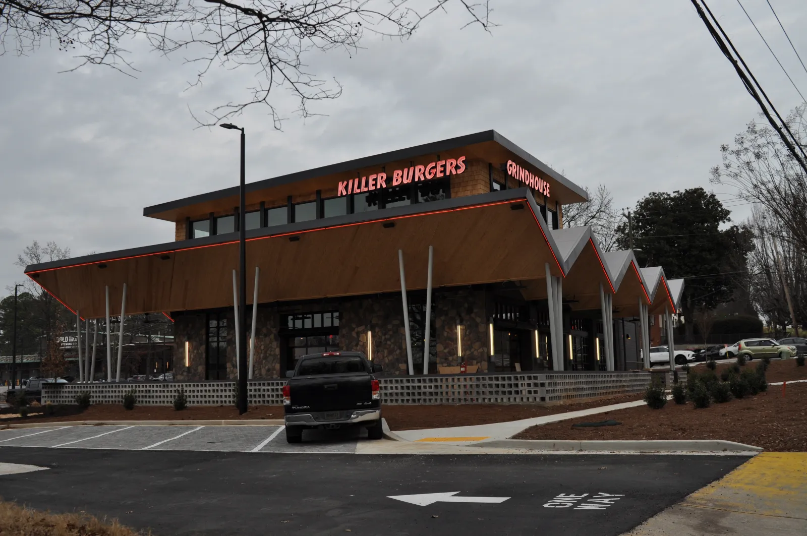 Modern Killer Burgers Grindhouse restaurant with unique angular roof and outdoor lighting at dusk.