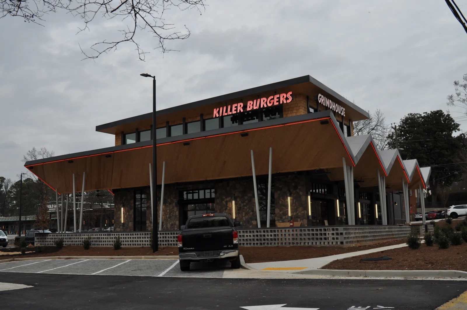 Modern Killer Burgers Grindhouse restaurant with distinctive angular roof and parking lot under cloudy sky.