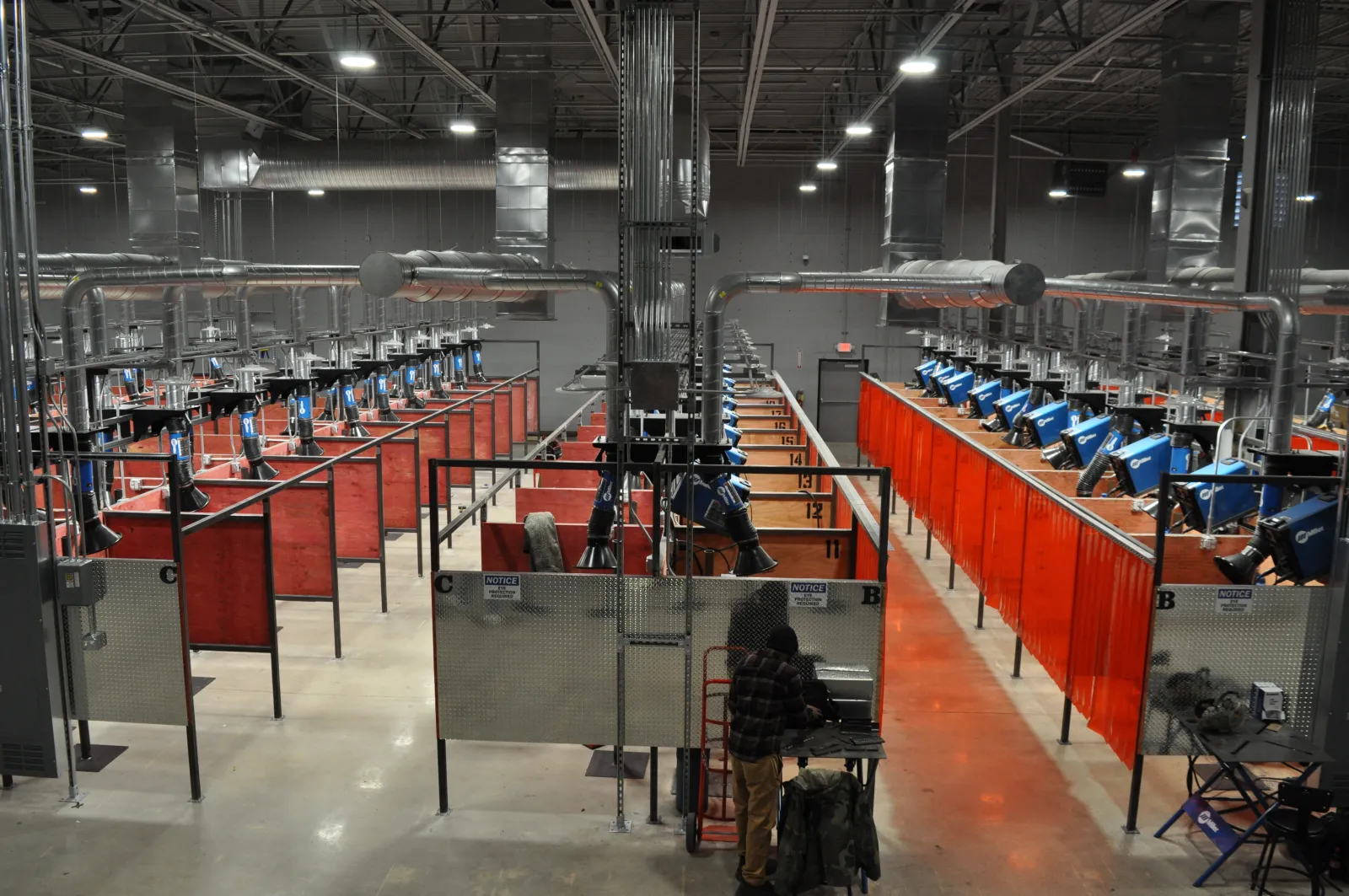 Industrial welding facility with multiple workstations separated by red curtains and ventilation systems overhead.
