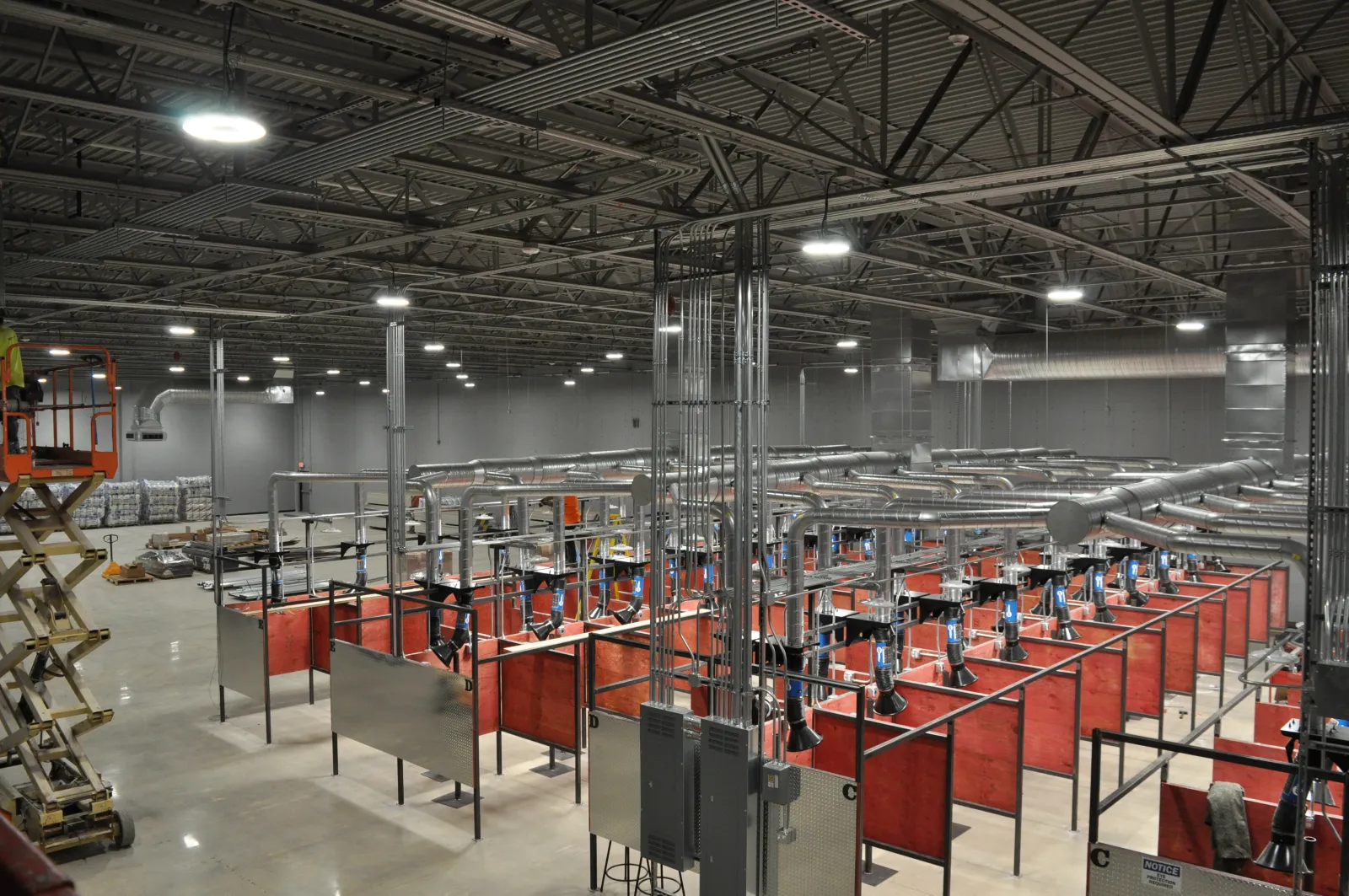 Industrial workshop with red welding booths and extensive ductwork under high ceiling lights in a spacious warehouse.