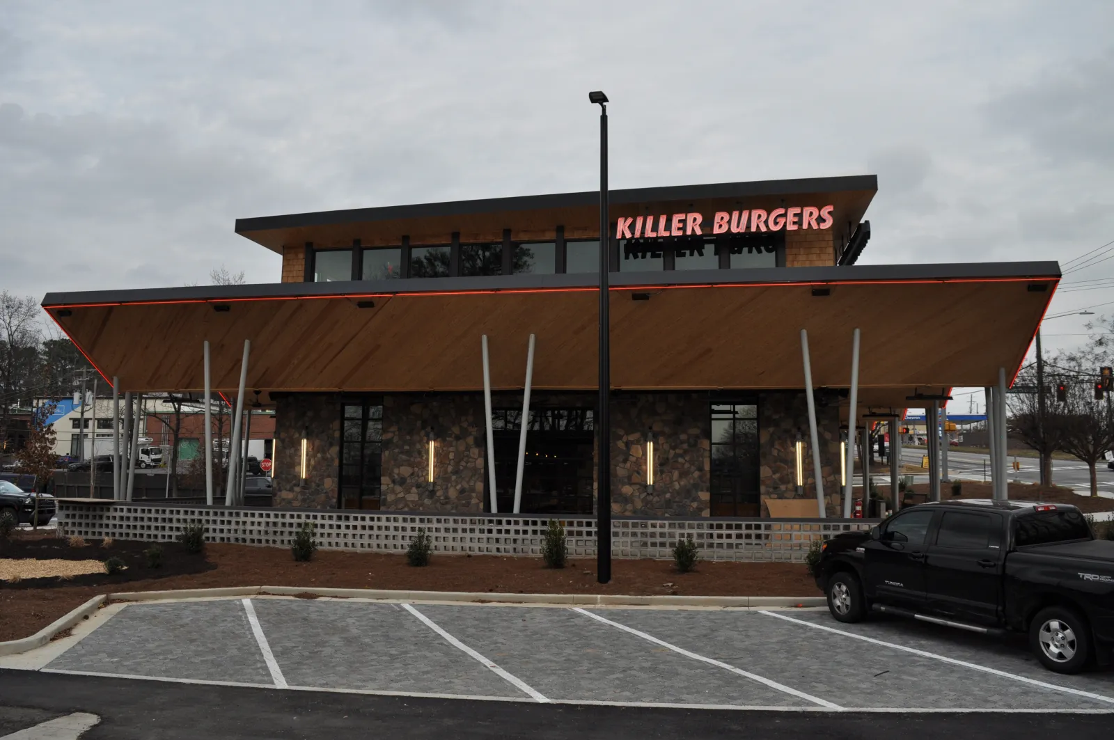 Modern Killer Burgers restaurant exterior with large wood awning and parking spaces under cloudy sky