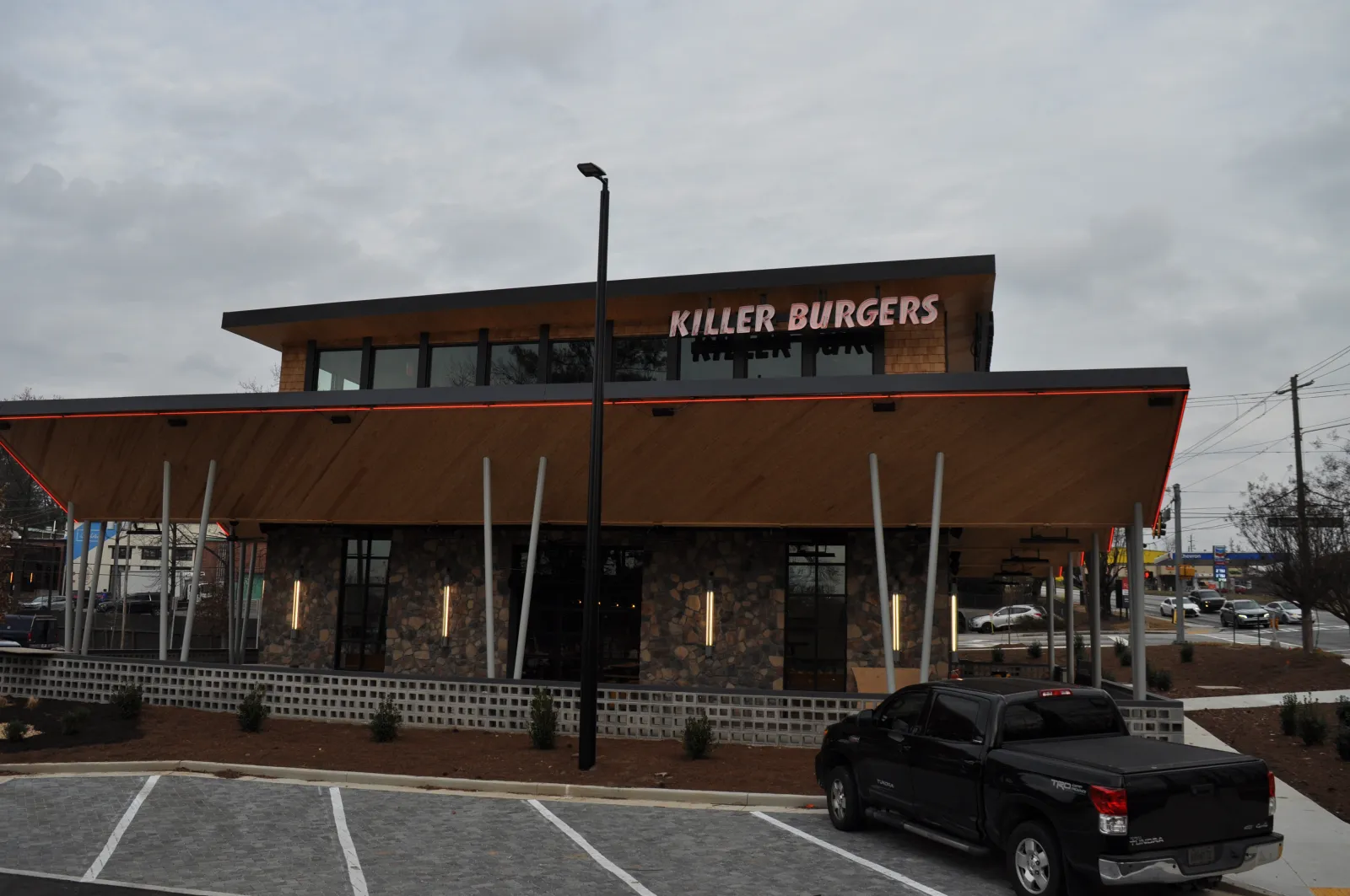 Modern Killer Burgers restaurant building with wood and stone facade and parked black pickup truck under overcast sky