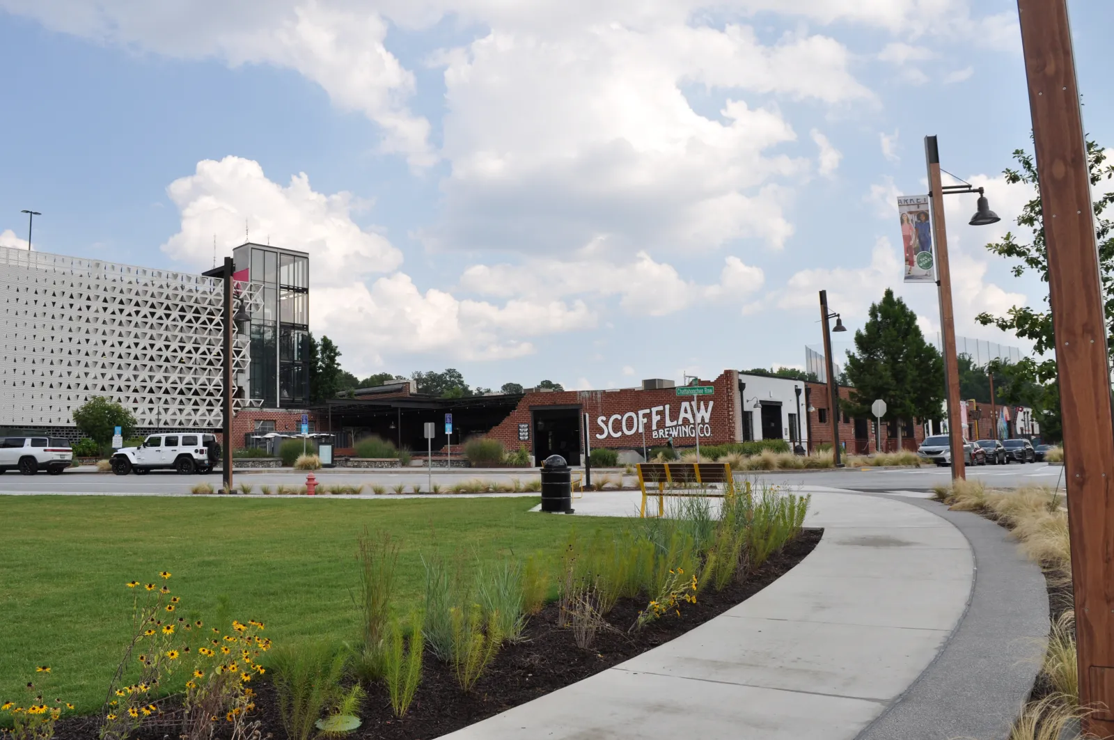Scofflaw Brewing Co building with grassy park and curved walkway under a partly cloudy sky.