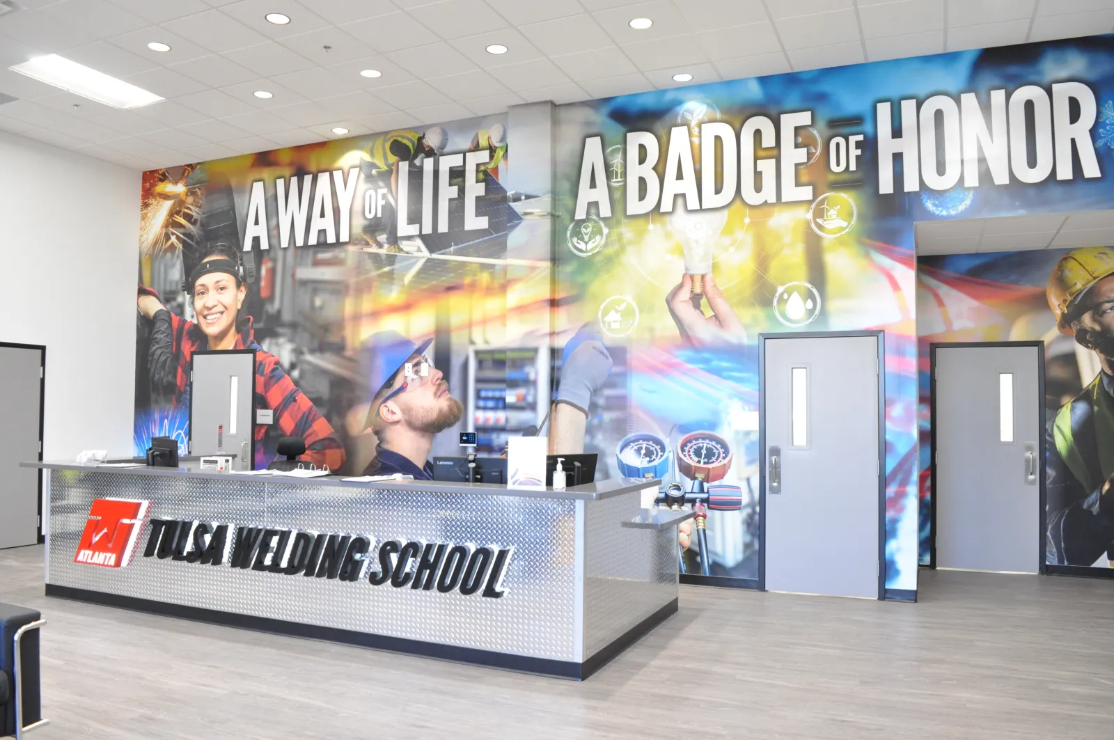 Reception area of Tulsa Welding School with large mural reading 'A Way of Life A Badge of Honor' and people welding images.