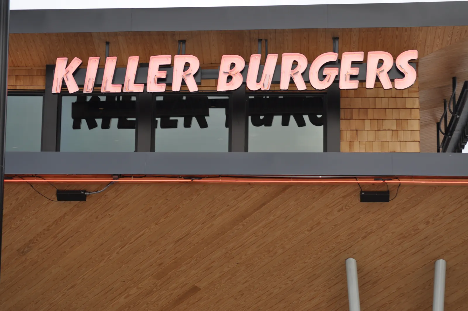 Killer Burgers restaurant sign with bold pink letters on wood panel exterior under an overhang.