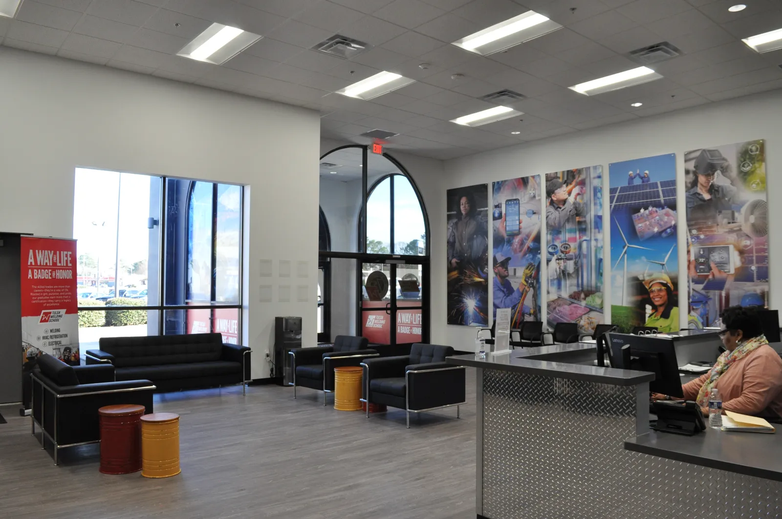 Modern office lobby with black sofas, colorful stools, large windows, and vibrant work-themed wall art.