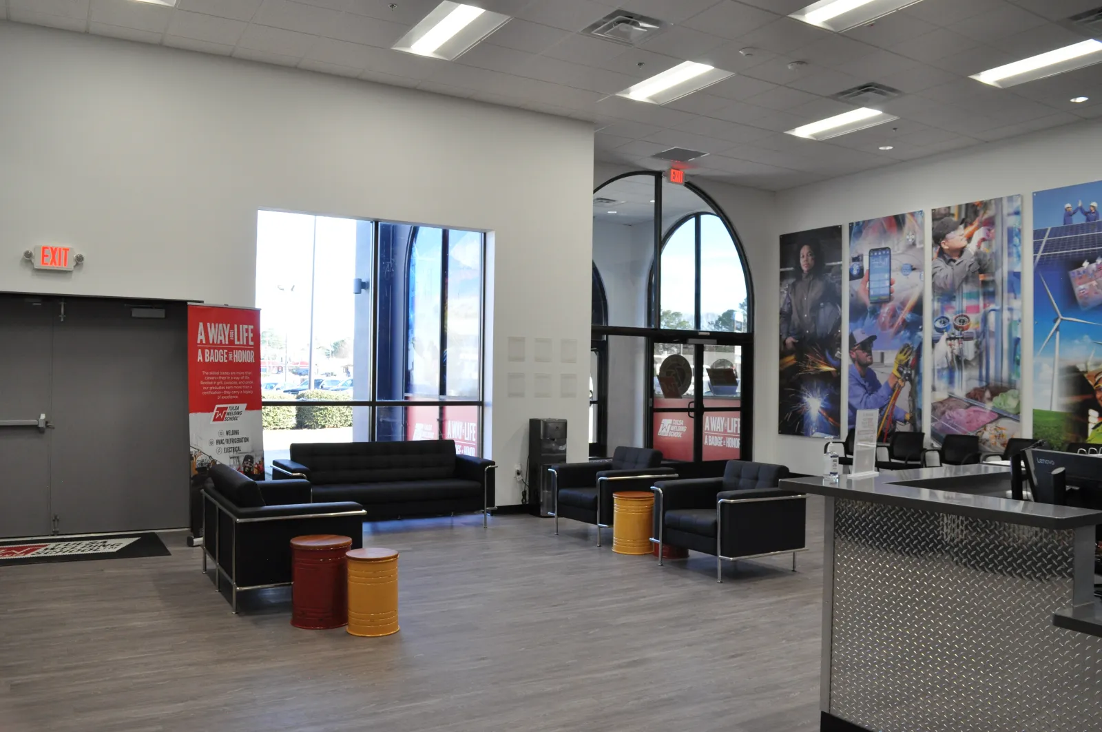 Modern lobby area with black sofas, colorful barrel stools, large windows, and vibrant wall murals advertising a trade organization.