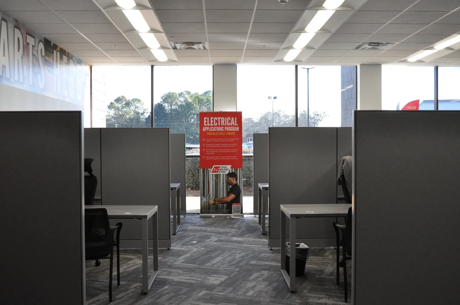 Modern study cubicles with chairs and a large window displaying an Electrical Applications Program sign outside.