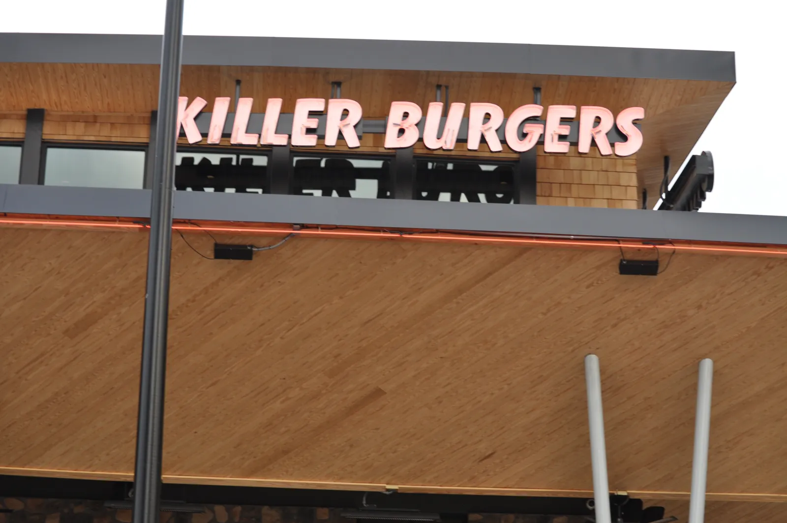 Killer Burgers restaurant sign with modern wooden and metal building facade under an overcast sky.