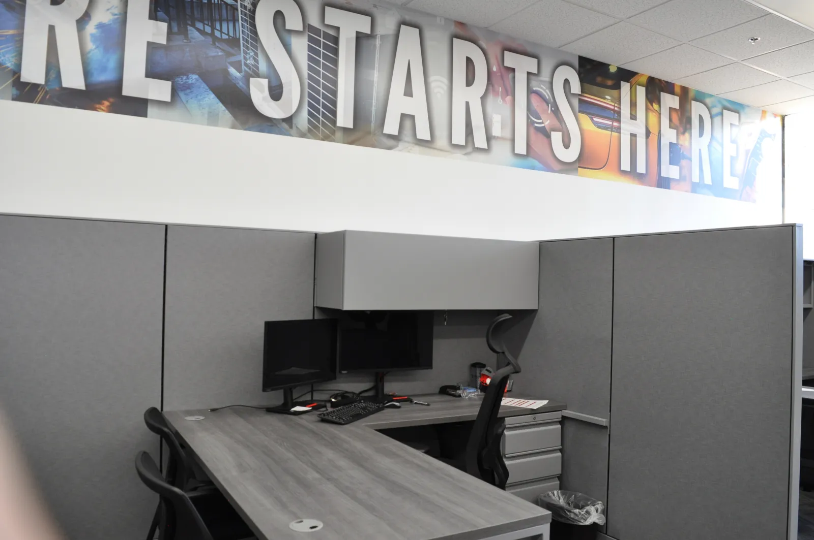 Modern office cubicle with dual monitors, ergonomic chair, and motivational RE STARTS HERE banner above