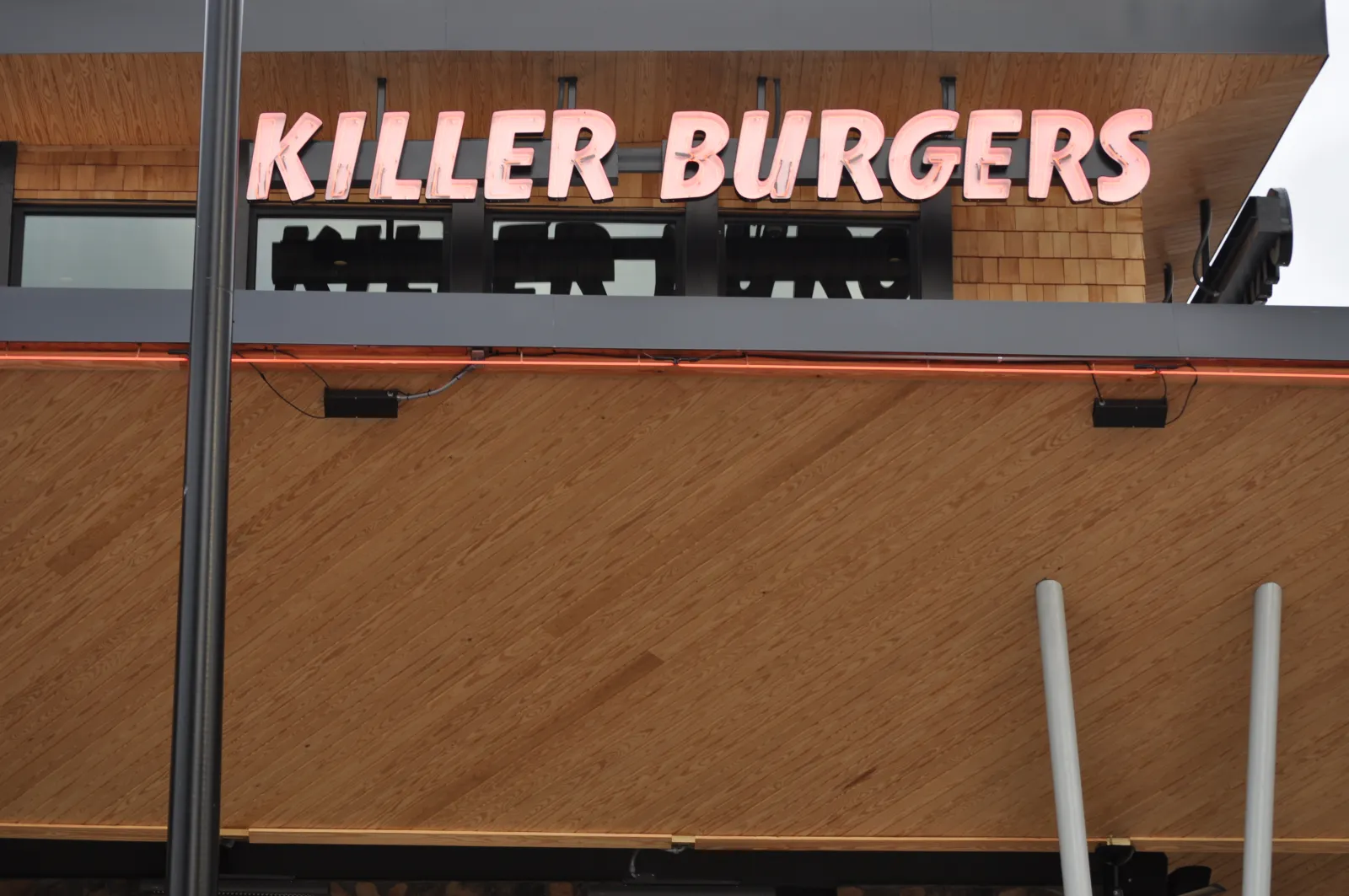 KILLER BURGERS restaurant sign with pink neon letters mounted on a wooden exterior wall.