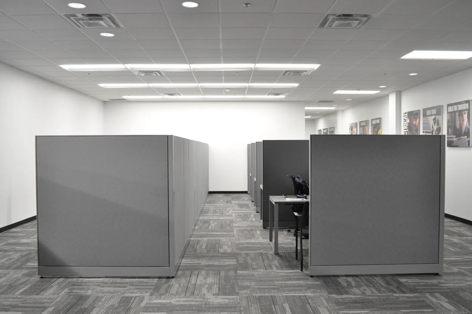 Empty modern office with gray cubicles, carpeted floor, and bright overhead lighting in a clean workspace.