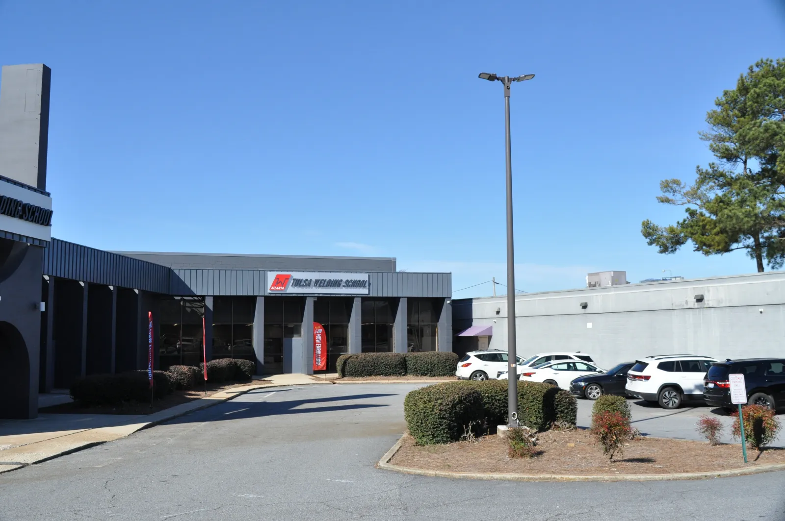 Front view of Tulsa Welding School building with parked cars and clear blue sky on a sunny day